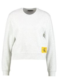 Sudadera gris recortada hecha de una mezcla de algodón, con puños y dobladillo de canalé, y una etiqueta amarilla que muestra el logo "CK" en el costado.