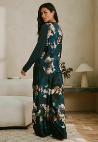 Blau- und teal-farbenes, blumenmusterndes Zweiteiler-Outfit mit langen Ärmeln und lockeren Hosen, aus einem leichten Stoff mit glatter Textur gefertigt.