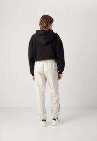 Musta lyhytcroppinen huppari, jossa on huppu, yhdistettynä vaaleanbeigeihin, resoripohjaisiin joggereihin ja valkoisiin lenkkikenkiin mustilla yksityiskohdilla. Takaviisto.
