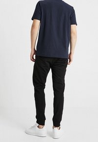 Navy cotton t-shirt with short sleeves and a round neckline, paired with black jogger pants and white sneakers, viewed from the back.