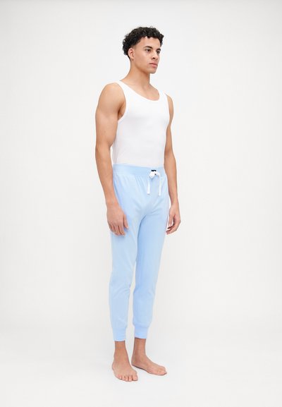 Lyseblå joggebukser med snor i livet og ribbestrikkede ermer, brukt sammen med en hvit tank topp. Stoffet ser mykt og lett ut.