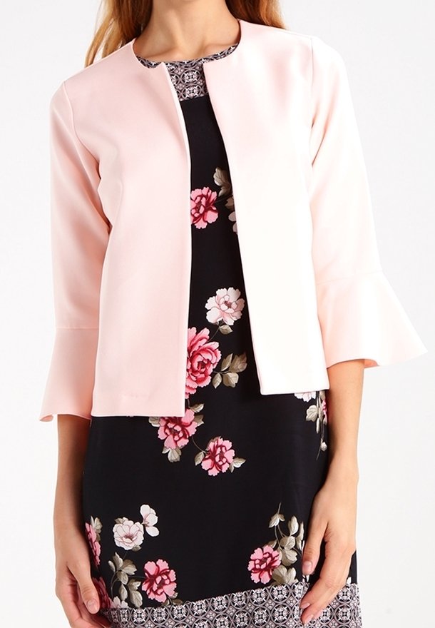 Jasnoróżowa, dopasowana kurtka z rękawami o długości trzech czwartych i subtelnym, lekko rozszerzanym mankietem, noszona na czarnej sukience w kwiaty z białymi i różowymi wzorami.