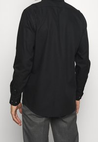 Svart långärmad skjorta med klassisk krage, mjuk textur och knappade manschetter, med rak ryggdesign och lätt kurvatur vid fållen.