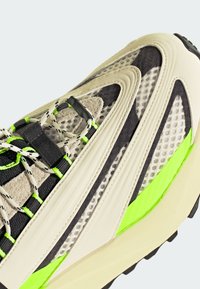 But sportowy wykonany z beżowych i czarnych materiałów, z panelami z siateczki, charakterystycznymi zielonymi akcentami, teksturowaną powierzchnią i unikalnym warstwowym wzorem.