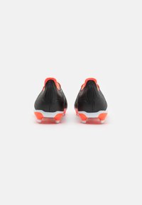 Botas de fútbol negras con acentos naranjas, que presentan un diseño elegante, superficie texturizada y una suela blanca con tacos moldeados.