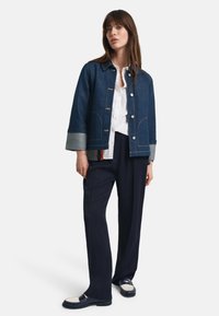 Denimjakke med knappelukking, marineblå med grå mansjetter, med to frontlommer og kontrastsøm. Kombinert med marineblå bukser og fottøy.