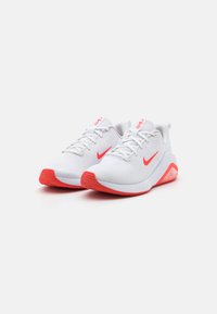 Baskets de sport blanches avec des accents rouges, dotées d'une tige en maille texturée, d'une semelle rembourrée et d'un logo signature sur le côté et la languette.