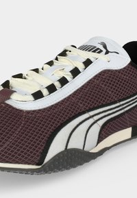 Κοντινό πλάνο σε βυσσινί αθλητικό παπούτσι Puma με λευκό και μαύρο λογότυπο, λευκά κορδόνια, υφασμένο πάνω μέρος και μαύρη καουτσούκ σόλα.