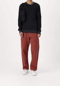 Maglione lavorato a maglia grigio scuro, pantaloni cargo color ruggine con tasche laterali e sneakers bianche. Piccola borsa a tracolla nera sulla spalla.