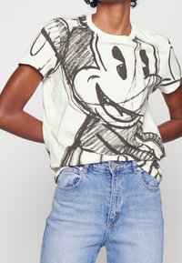 Hvid bomulds T-shirt med et stort sort grafisk design. Rund halsudskæring og korte ærmer. Sammen med lyseblå denim jeans.