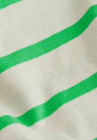 Bawełniana tkanina w naprzemiennie występujące zielone i białe paski. Tekstura jest miękka i gładka, podkreślając wyraźny kontrast kolorów w wzorze.