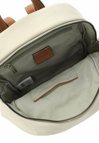 Cremefarbener Rucksack mit braunen Lederelementen. Innen aus hellgrünem Stoff ausgekleidet, mit einer Reißverschlusstasche und einem Kartenhalter.