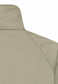 Épaule de veste beige avec col montant et coutures visibles sur un tissu clair, sans caractéristiques ni motifs supplémentaires.