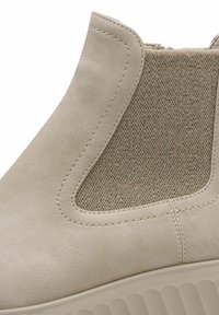 Bottine Chelsea beige avec panneau latéral élastique texturé, dessus lisse, coutures détaillées et semelle en caoutchouc.