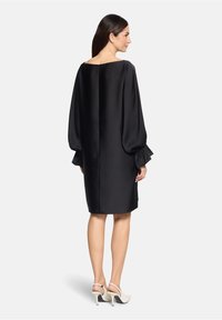 Czarna satynowa sukienka z długimi, obszernymi rękawami i kwadratowym dekoltem. Posiada zamek błyskawiczny z tyłu i sięga powyżej kolan.