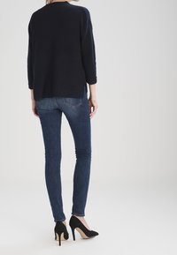 Navy ribbed sweater with three-quarter sleeves, paired with dark blue skinny jeans. Model wears black high heels with beige accents.