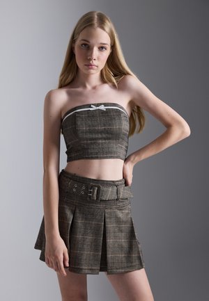 Braun karierter Zweiteiler bestehend aus einem schulterfreien Crop-Top mit weißem Bogen und einem plissierten Minirock mit tailliertem Bund und silbernen Hardware-Details.