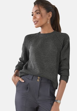 Dark grey knitted sweater with ribbed details, round neckline, and relaxed fit, paired with navy high-waisted trousers and a wristwatch.