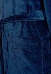 Marineblauer Velours-Bademantel mit strukturiertem Finish, ausgestattet mit einem gebundenen Gürtel und einer Seitentasche, verziert mit einem gestickten Logo.