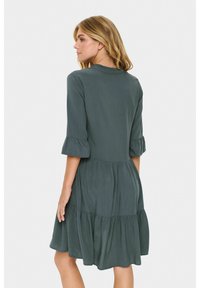 Rochie verde închis, până la genunchi, cu mâneci până la 3 sferturi, decolteu rotund, accente volan și fustă în straturi dintr-un material fluid.