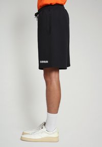 Pantaloni sportivi neri realizzati in tessuto morbido, con tasche laterali e un logo stampato vicino all'orlo. Abbinati a sneakers bianche e calze a righe.