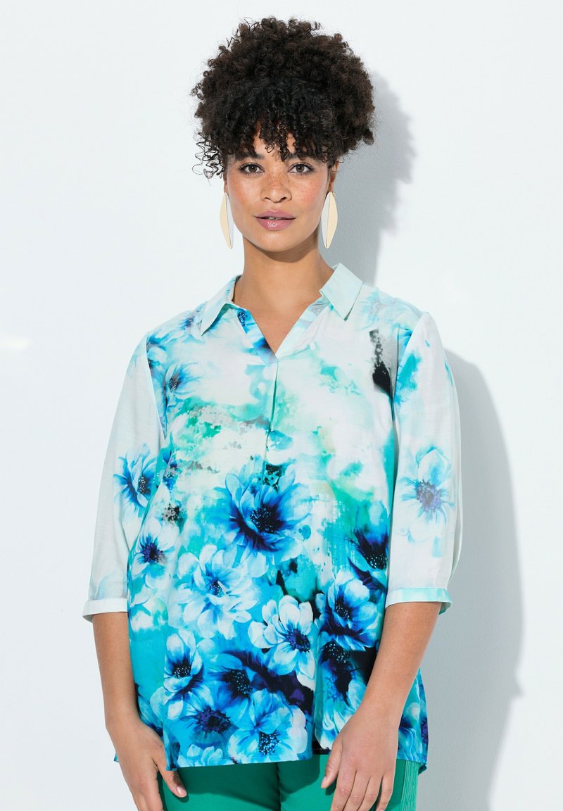 Blusa floreale in tonalità di blu e bianco, dotata di colletto e maniche a tre quarti. Tessuto leggero con una consistenza morbida.