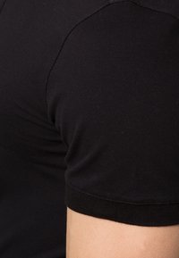 T-shirt en coton noir avec un col rond et des manches courtes. Le tissu a une texture lisse, montrant un gros plan de la couture et de l'ajustement.