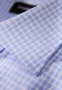 Niebiesko-biała tkanina w kratkę z kołnierzykiem w szpic, o gładkiej fakturze i starannym przeszyciu na krawędziach.