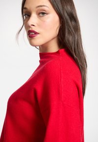 Roter Wollpullover mit hohem Kragen, langen Ärmeln und einer strukturierten Oberfläche. Bietet eine lockere Passform und auffällige Nahtdetails.