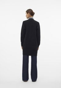 Maglione nero con maniche lunghe, collo alto e un texture in maglia, abbinato a jeans in denim scuro a gamba larga. Retro, design minimalista.