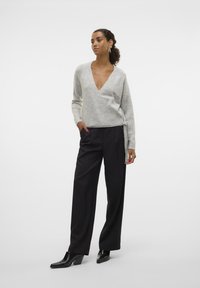 Light gray wool-blend wrap sweater with a deep V-neck, paired with high-waisted black trousers and black pointed ankle boots.