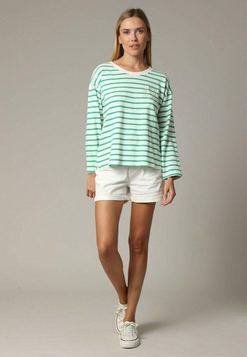 Haut à manches longues rayé vert et blanc avec une coupe décontractée, associé à un short blanc. Le tissu semble doux ; style décontracté avec un col rond.