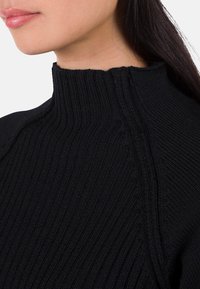 Schwarzer Strickpullover mit hohem geripptem Kragen und strukturiertem Muster, ausgestattet mit einer taillierten Passform und sichtbaren Nahtdetails.