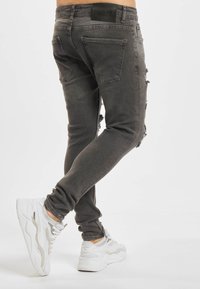 Grå smale jeans av denim, med slitte detaljer, fem lommer og en svart etikett på midjebåndet. Kombinert med hvite joggesko.