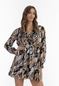 Langärmliges Kleid aus schwarz-weißer und gold gemusterter Stoff, mit Rüschen, einem V-Ausschnitt und einem gestuften Rock. Glatte und leichte Textur.