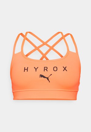 Sujetador deportivo de un brillante color naranja con tirantes entrelazados, que presenta el texto "HYROX" y un logo negro de Puma en la parte frontal. Textura suave, diseño ajustado.