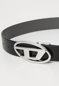 Black leather belt with a silver oval buckle featuring a geometric cutout. The belt has small adjustment holes along its length.