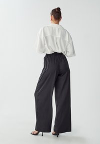 Bijela oversized bluza kratkih rukava, uparena s labavim crnim satenskim hlačama s elastičnim pojasom. Crne sandale na visoku petu upotpunjuju izgled.