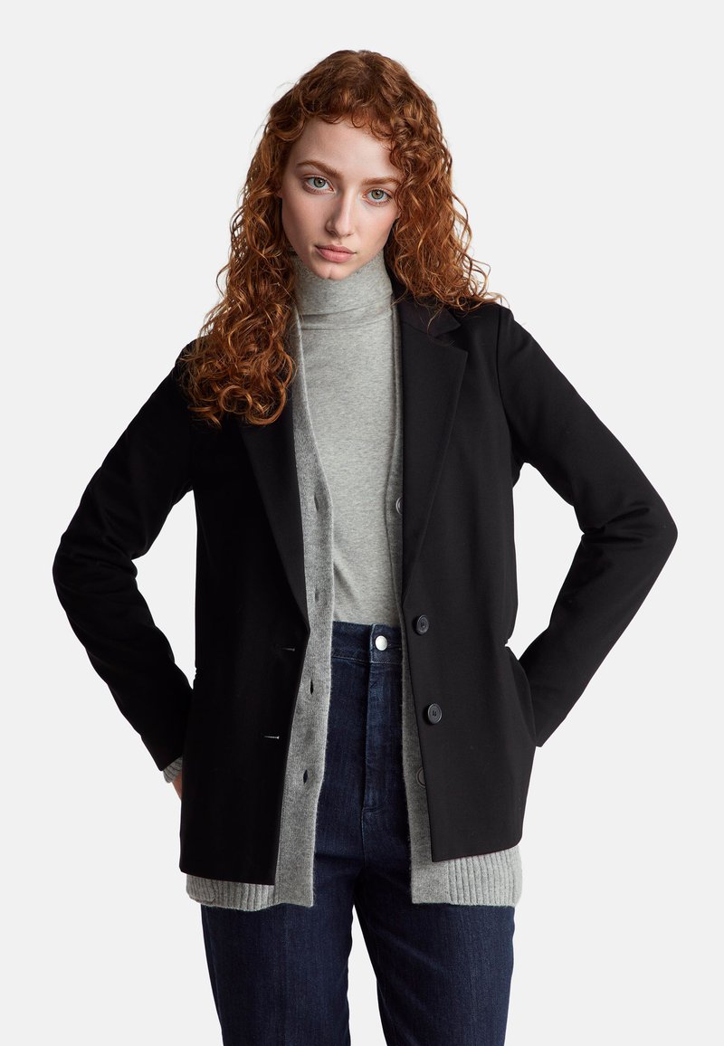 Černé sako se strukturovaným designem, spárované se světle šedým rolákem a tmavými džíny. Texturovaná tkanina s knoflíkovými detaily.