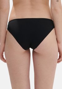 Fondo di bikini nero con un design a vita bassa, texture liscia e copertura minima. I lati sono tagliati leggermente più in alto per un look moderno.