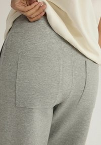 Szare dresowe spodnie o miękkiej fakturze, z dwoma tylnymi kieszeniami i dopasowanym paskiem w talii. Materiał jest gładki i ma casualowy fason.