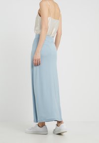 Ljust blå vida byxor i mjukt tyg med en slät midja, ihop med vita sneakers och en sidentopp.