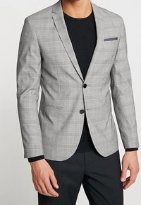 Grå rutigt blazer med notch lapels, en knapp och en bröstficka. Bärs över en svart crew neck-top, ihop med mörka byxor.