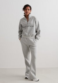 Grey fleece zip-up sweatshirt with black lettering, paired with matching grey sweatpants. Soft texture, relaxed fit, and casual style.