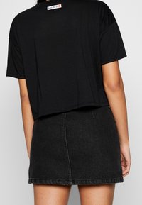 Czarna krótka koszulka z krótkim rękawem i napisem "Just do it." z tyłu, zestawiona z ciemnoniebieską mini spódnicą dżinsową.