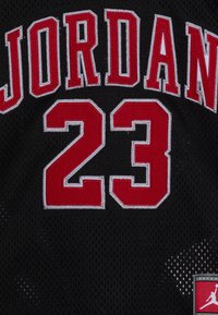Czarna koszulka sportowa z czerwonym i białym napisem "JORDAN" oraz numerem 23 w wyraźnych, haftowanych literach, z małą naszywką Jumpman.
