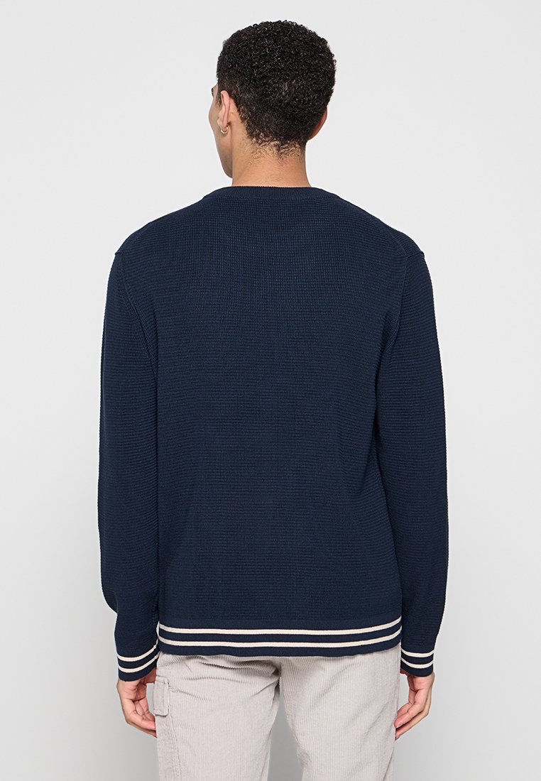 Marineblaue Strickjacke mit langen Ärmeln und gerippten Bündchen. Sie hat einen runden Halsausschnitt und kontrastierende cremefarbene Streifen am Saum und an den Bündchen.