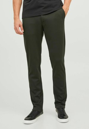 Slim-fit, donkergroene broek van glad, lichtgewicht materiaal. Beschikt over zijzakken en een eenvoudig ontwerp, gecombineerd met zwarte sneakers.