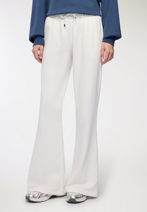 Pantaloni della tuta bianchi a campana con vita elasticizzata e lacci. Tessuto morbido con una consistenza liscia; abbinati a sneaker argentate.