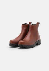 Paar braune Leder-Stiefel mit schwarzem Profilsohle und seitlichem Reißverschluss auf weißem Hintergrund.